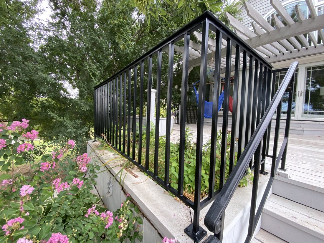 Black deck railing surrounded by garden plants.